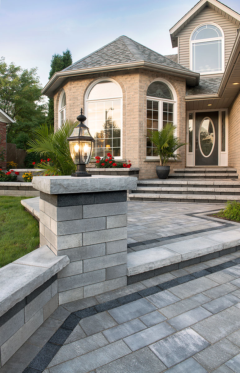 Paver driveway and stone pillar with lantern at an elegant home entry