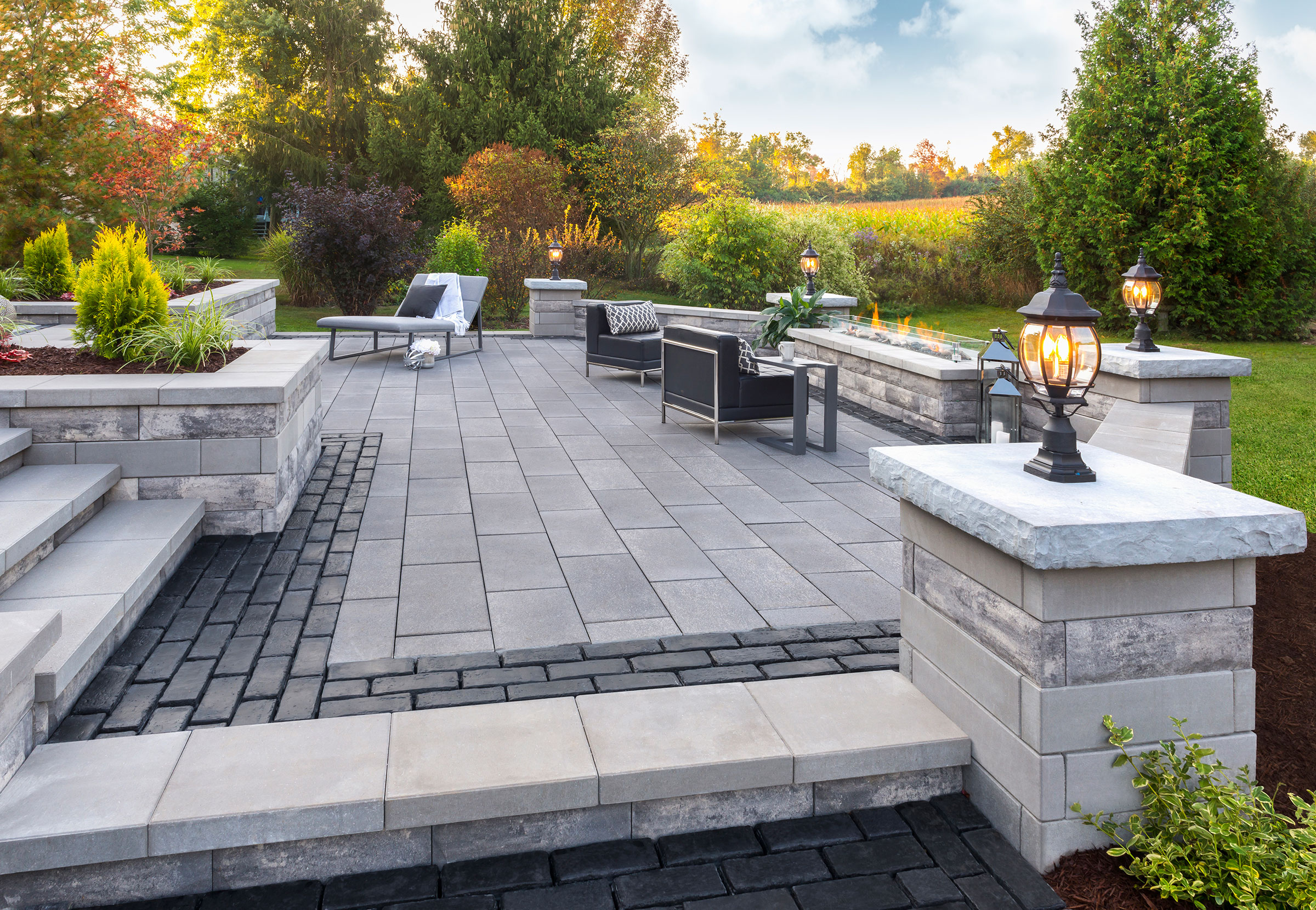 Elevated paver patio with pillar lighting and fire table at golden hour